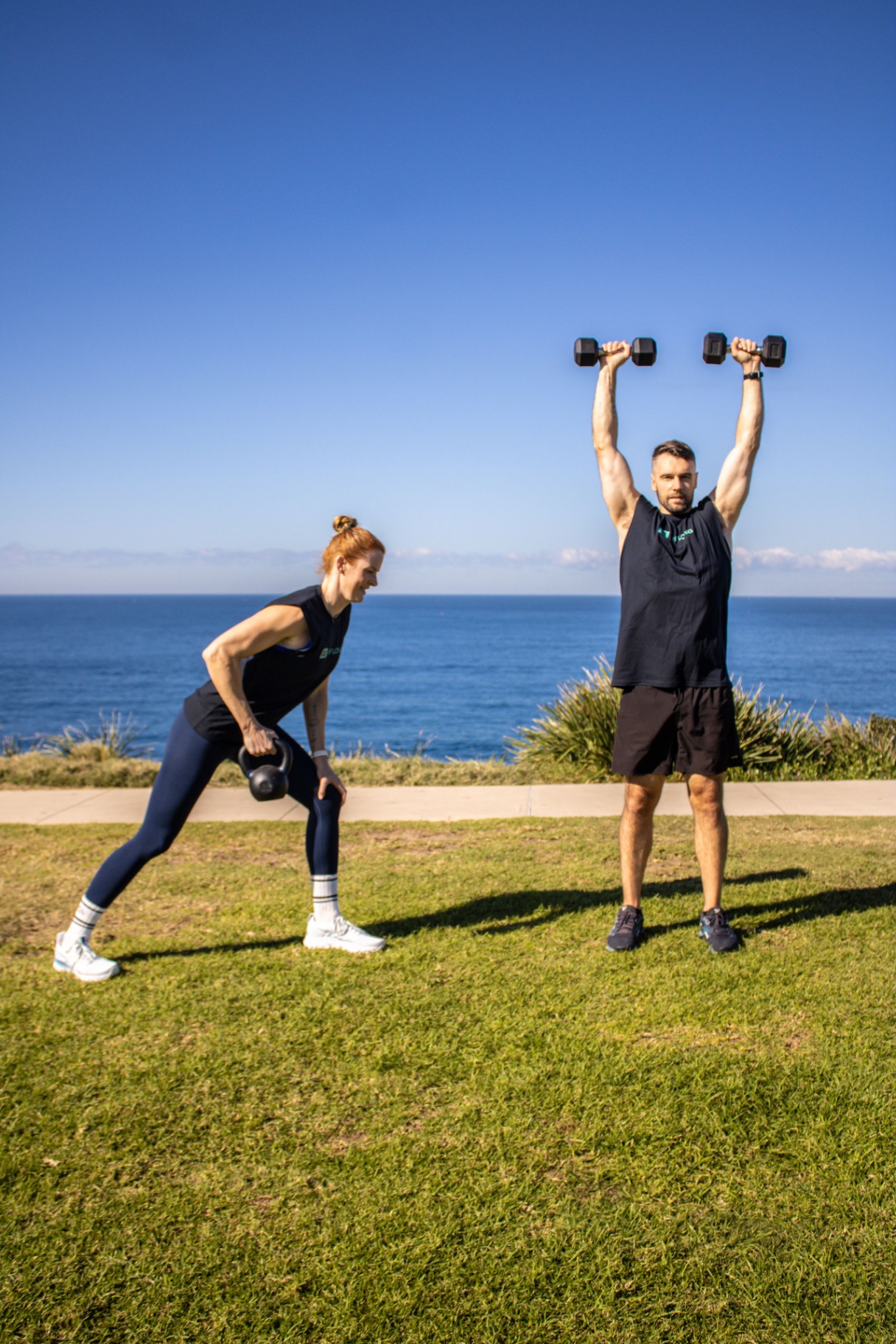 Michael and Jade training with a kettlebell and dumbbells by the ocean